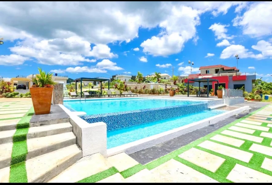 The swimming pool on a bright day, framed by stone steps, planters and green lawns